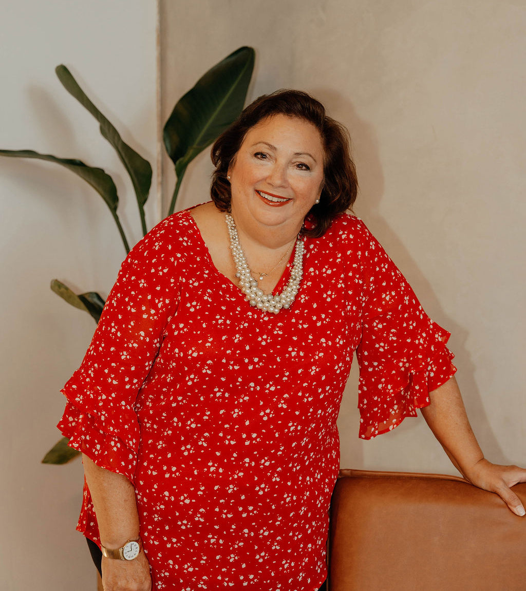 Mary Kelly of The Workplace Community Podcast in a red dress with white patterns standing indoors against a neutral wall.