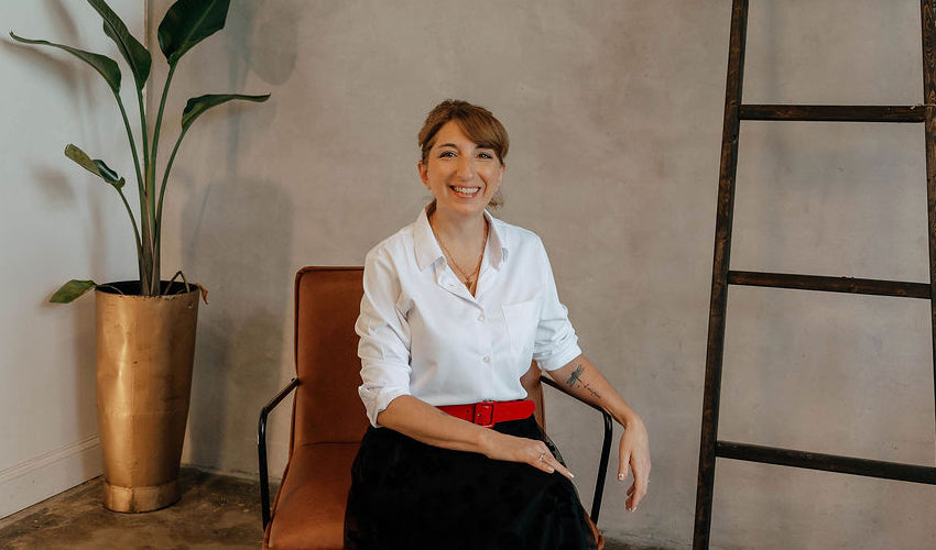 Nichole Maniscalco of The Workplace Community Podcast sitting on a chair in a room with a plant and ladder.