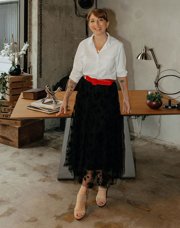 Nichole Maniscalco of The Workplace Community Podcast in a white shirt and black skirt standing in an office setting.
